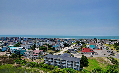 A coastal town with colorful houses and buildings, green lawns, and roads, set near the shoreline with the ocean visible in the background under a clear blue sky—perfect for a relaxing stay at a Sunset Beach NC bed and breakfast.