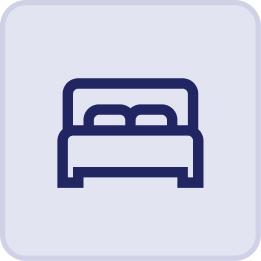 Simple icon of a bed with a headboard and two pillows, depicted in dark blue on a light background with rounded corners—evoking the comfort of the Hatteras Grand Room at Sunset Inn.