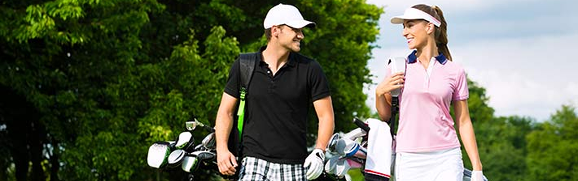 A man and woman dressed in golf attire walk on a golf course, smiling at each other and carrying golf bags—one of the top things to do in Sunset Beach NC. Lush green trees and grass fill the scenic background.