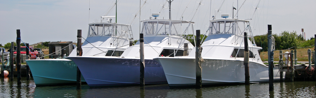 Three motor yachts are docked side by side at a marina, with calm water in the foreground and trees and buildings visible in the background—a perfect scene among the many relaxing things to do in Sunset Beach NC.