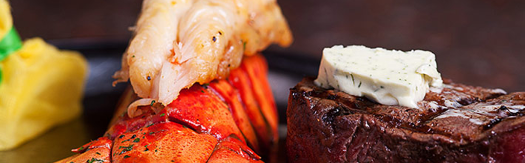 Close-up of a surf and turf dish featuring lobster tail and grilled steak topped with herb butter, with a yellow side in the background—a delicious highlight among things to do in Sunset Beach NC.