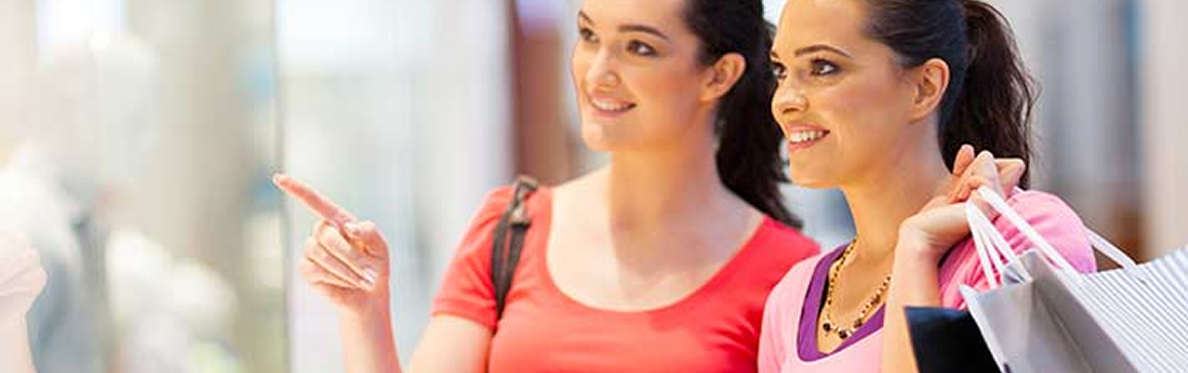Two women smiling and shopping, one holding shopping bags and the other pointing ahead, both appearing happy and engaged—discovering fun things to do in Sunset Beach NC in a brightly lit indoor setting.